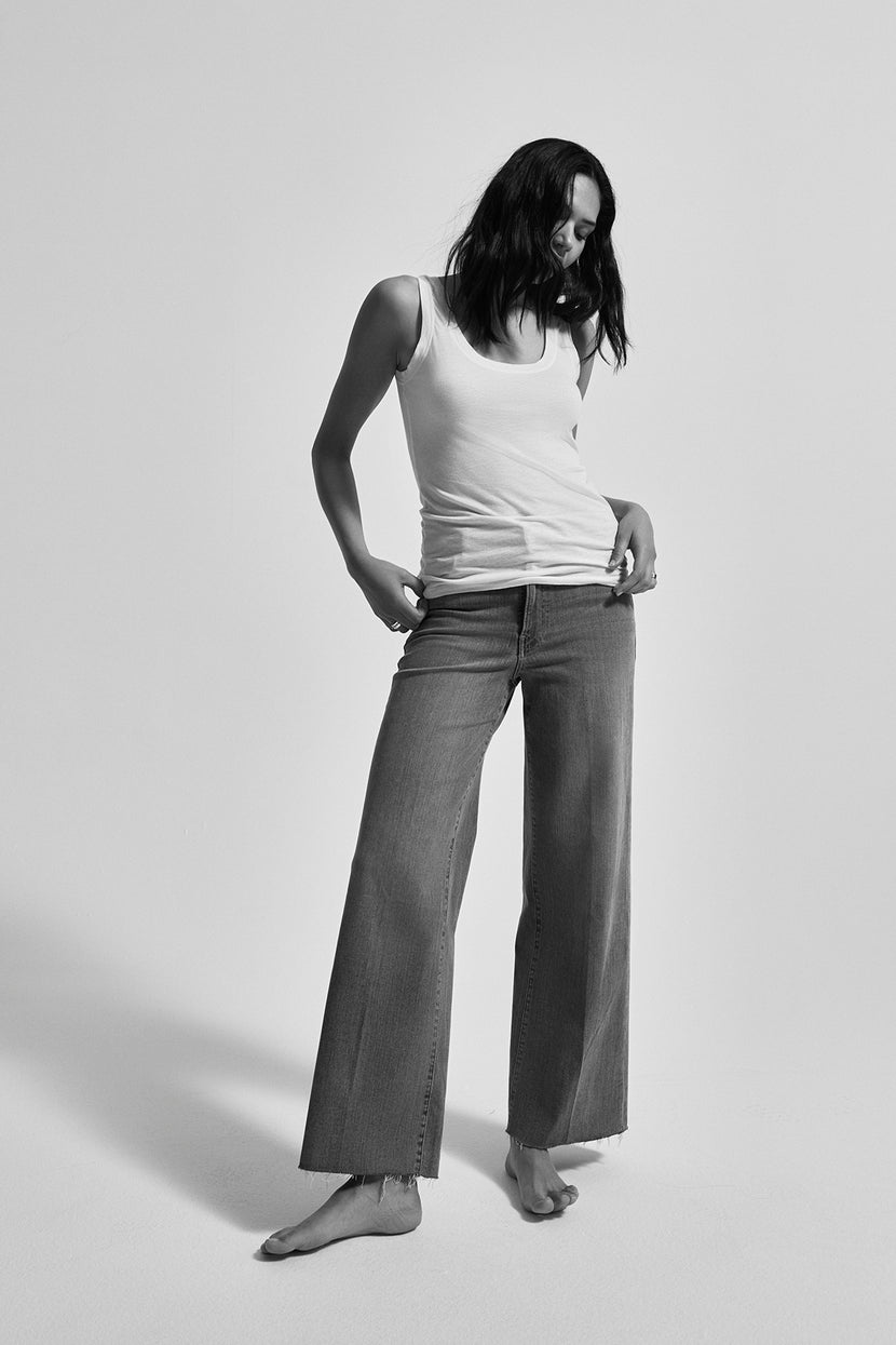 A black and white photo captures a person standing barefoot, hands in pockets, wearing a gauzy MOSSY TANK TOP by Velvet by Graham & Spencer paired with loose-fitting jeans—a versatile wardrobe addition.