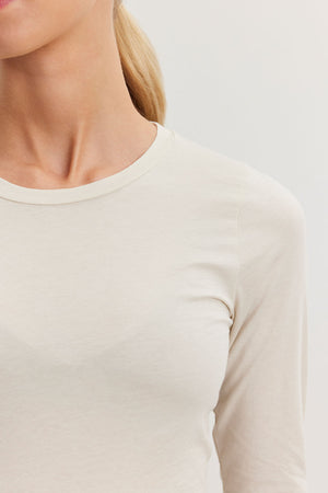 A person wearing the ZOFINA TEE by Velvet by Graham & Spencer—an ultra-soft gauzy whisper beige fitted long sleeve tee with a classic crew neckline—has her blonde hair tied back neatly against a neutral background.