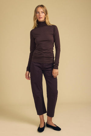 A person wearing a brown long-sleeve turtleneck and BRYLIE PANT cropped dark brown barrel leg pants with utilitarian patch pockets, paired with black flats.