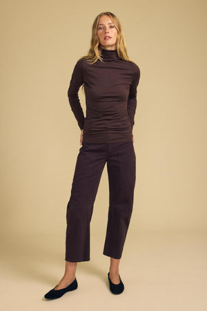 A person wearing a long-sleeved dark brown turtleneck top and BRYLIE PANT cropped barrel leg pants with utilitarian patch pockets.