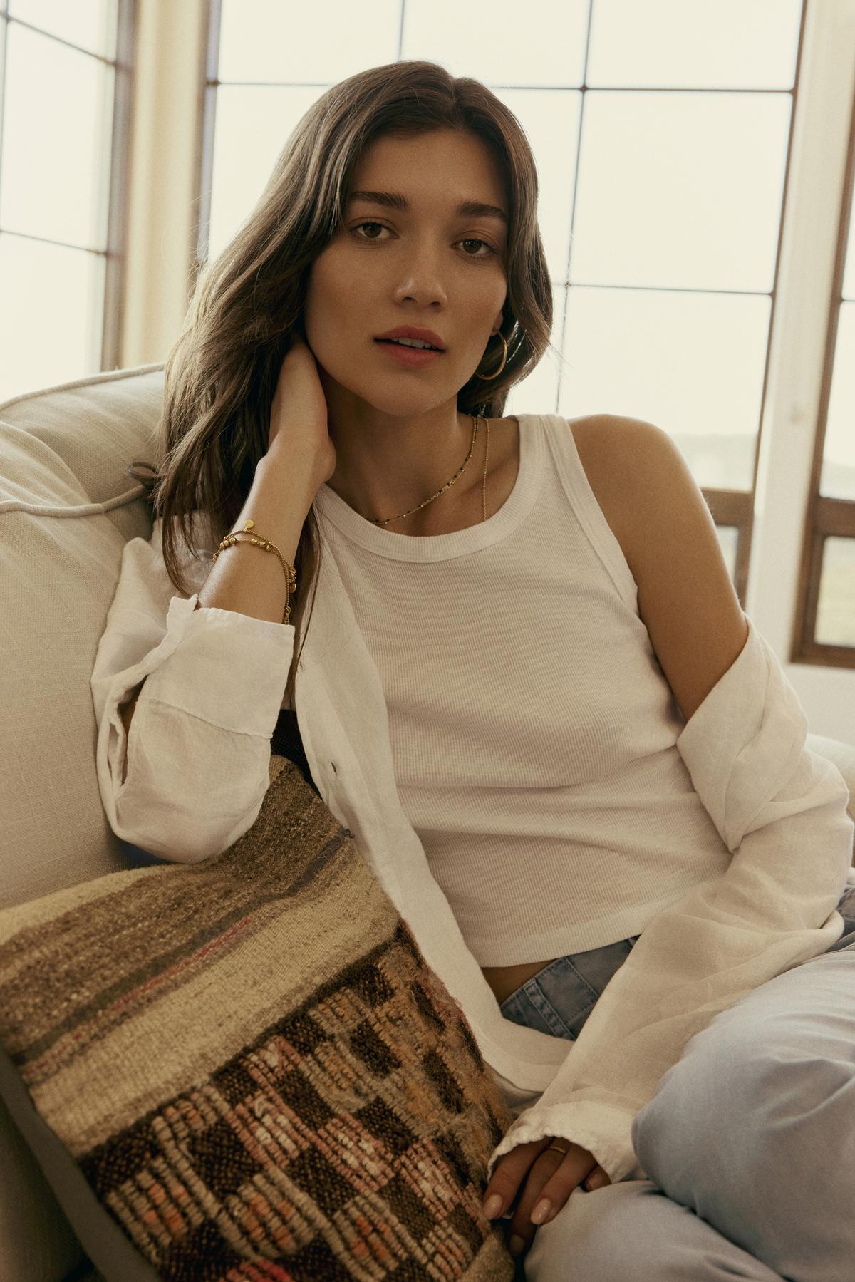 Woman in a Velvet by Graham & Spencer HARLA RIBBED CROPPED TANK TOP and open shirt posing casually while seated, resting her chin on her hand, soft natural lighting.-36443629617345