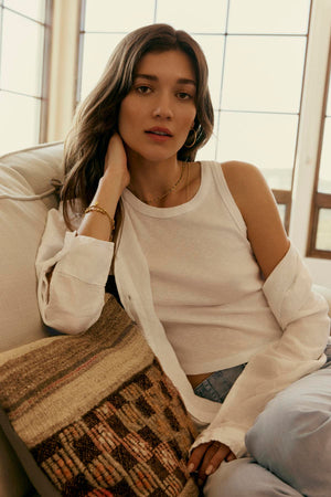 Woman in a Velvet by Graham & Spencer HARLA RIBBED CROPPED TANK TOP and open shirt posing casually while seated, resting her chin on her hand, soft natural lighting.