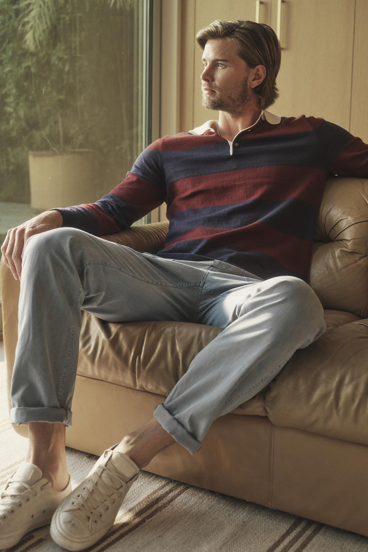 A man sitting on a couch wearing a Velvet by Graham & Spencer Hastings Striped Polo Sweater and jeans.-26768010969281