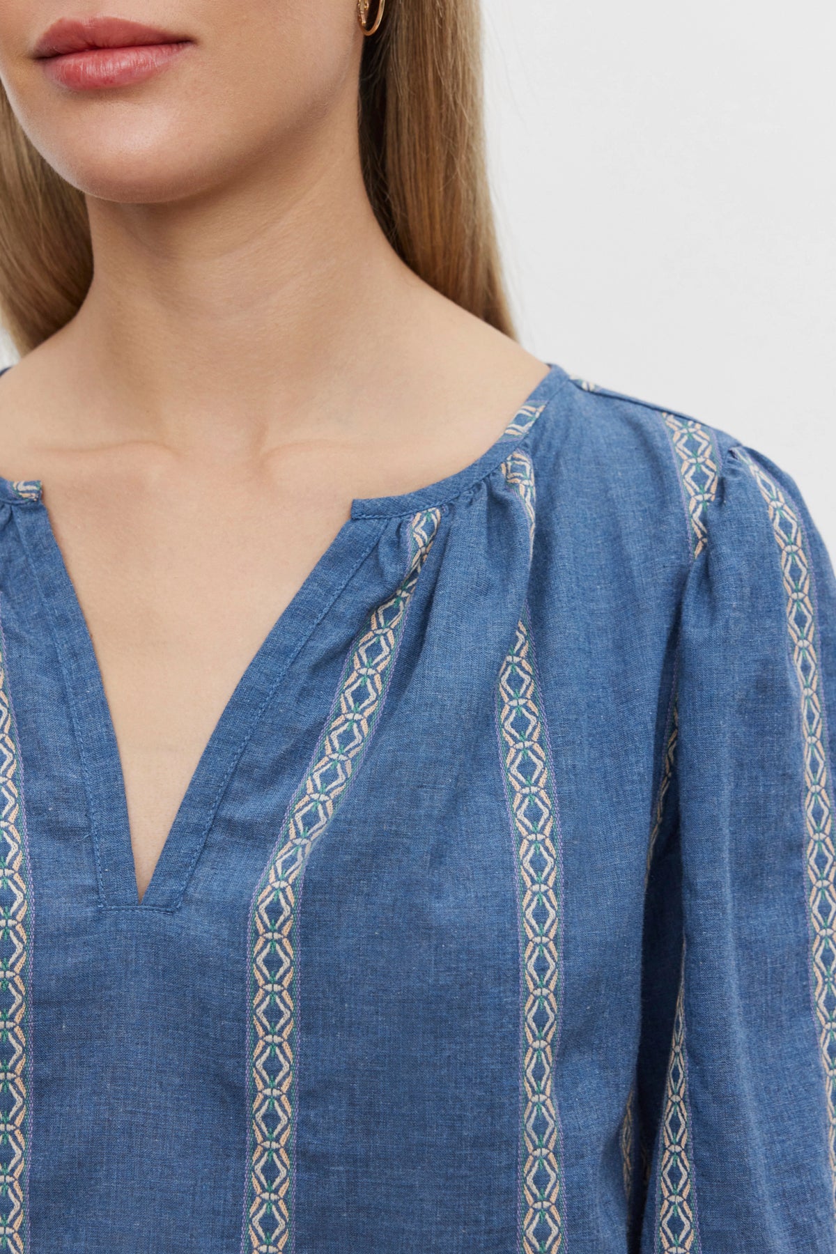   A person wearing the RAYLEE TOP by Velvet by Graham & Spencer, a relaxed fit blue split neck shirt with patterned vertical stripes. Only the lower half of their face and upper chest are visible. 