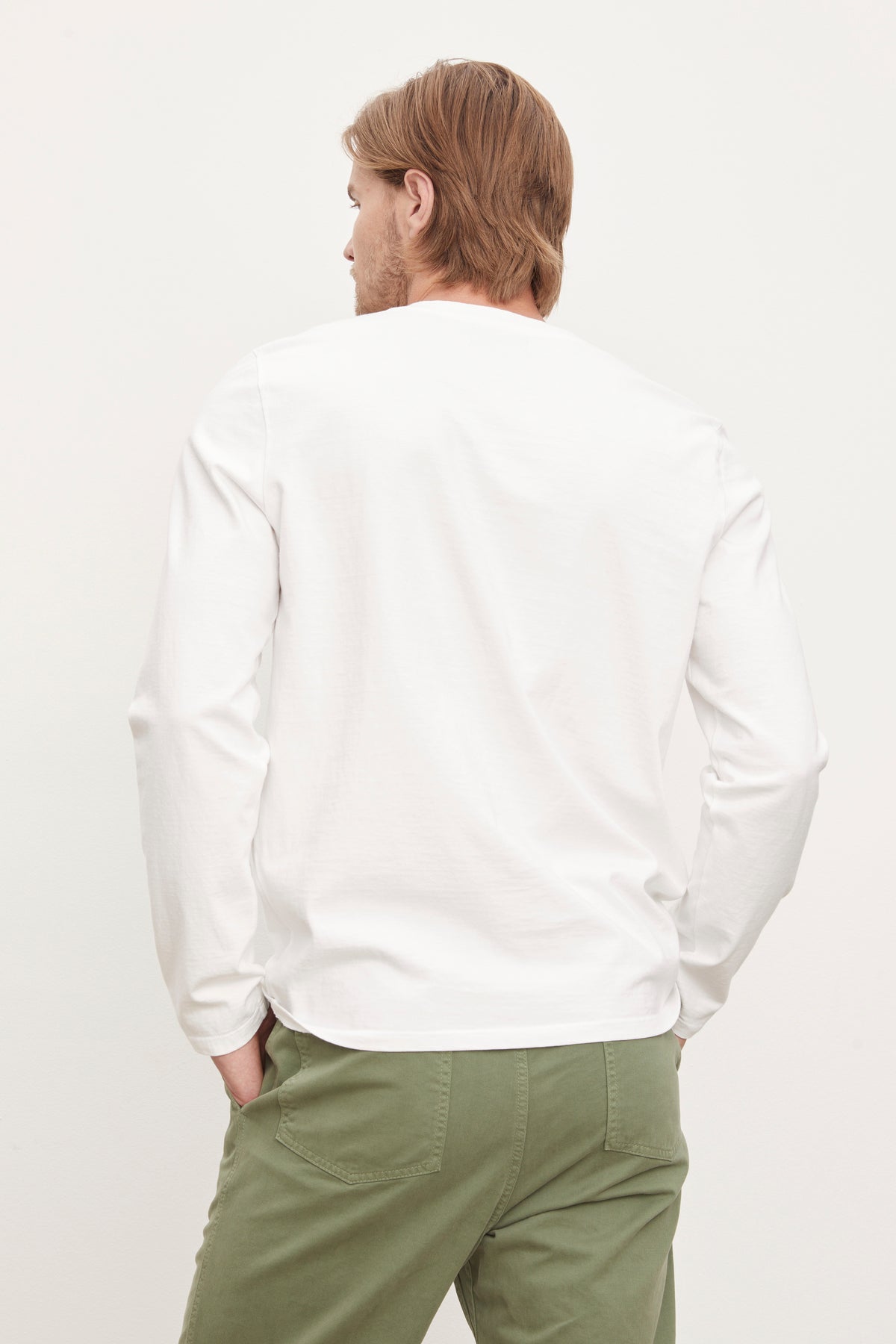   Man viewed from behind, wearing a white long-sleeve cotton jersey Holt Henley by Velvet by Graham & Spencer with a four-button placket and olive green pants, standing against a plain background. 