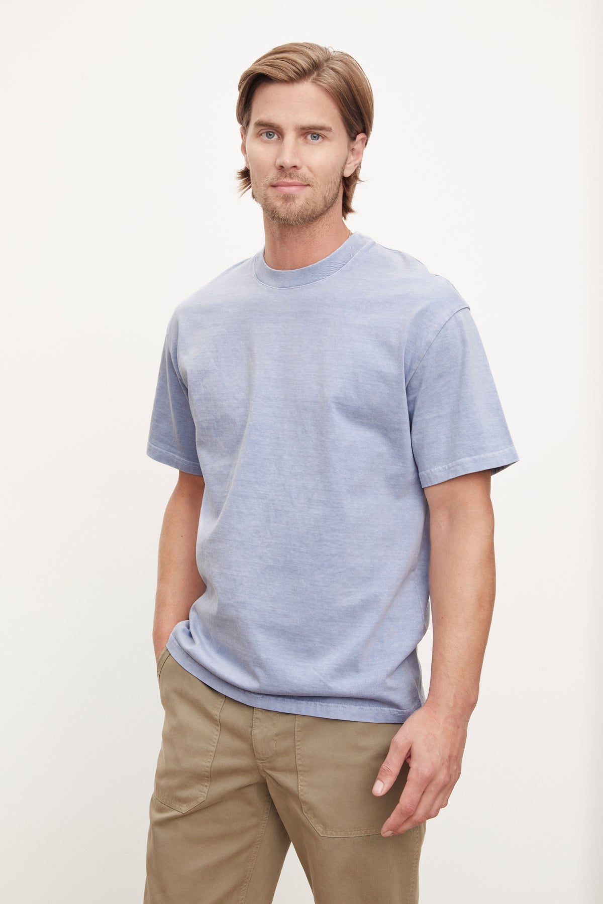   A man in a relaxed fit, plain blue cotton JACOBI HEAVY JERSEY CREW NECK TEE and khaki pants standing against a white background by Velvet by Graham & Spencer. 