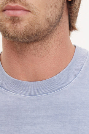 Close-up of a man with stubble wearing a versatile, blue cotton Velvet by Graham & Spencer Jacobi Heavy Jersey Crew Neck Tee with a relaxed fit.