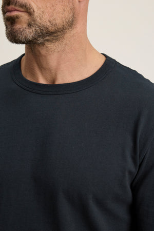 A close-up of a man's lower face and upper torso wearing the BRADY TEE by Velvet by Graham & Spencer in dark midweight jersey, with a short beard visible—ideal for everyday wear.
