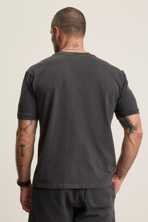 A man with short hair, tattoos, and a necklace is seen from behind wearing the ELIAS TEE by Velvet by Graham & Spencer—a plain dark gray heavy jersey crewneck t-shirt paired with matching pants for an everyday staple look.