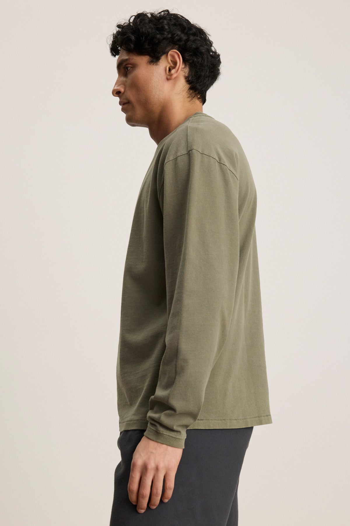 A man in profile wears the Velvet by Graham & Spencer FINNICK TEE in olive green—a heavyweight jersey with a ribbed crew neckline—paired with dark pants, set against a plain light background.-40452482531521