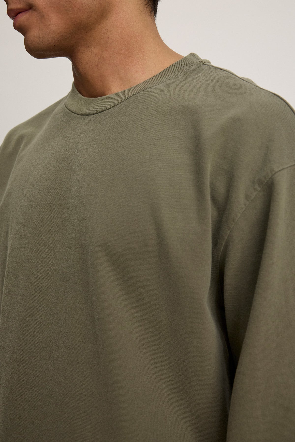 A person is shown from neck to mid-torso, facing partially left, wearing the Velvet by Graham & Spencer FINNICK TEE in olive green with long sleeves and a ribbed crew neckline.-40452482498753