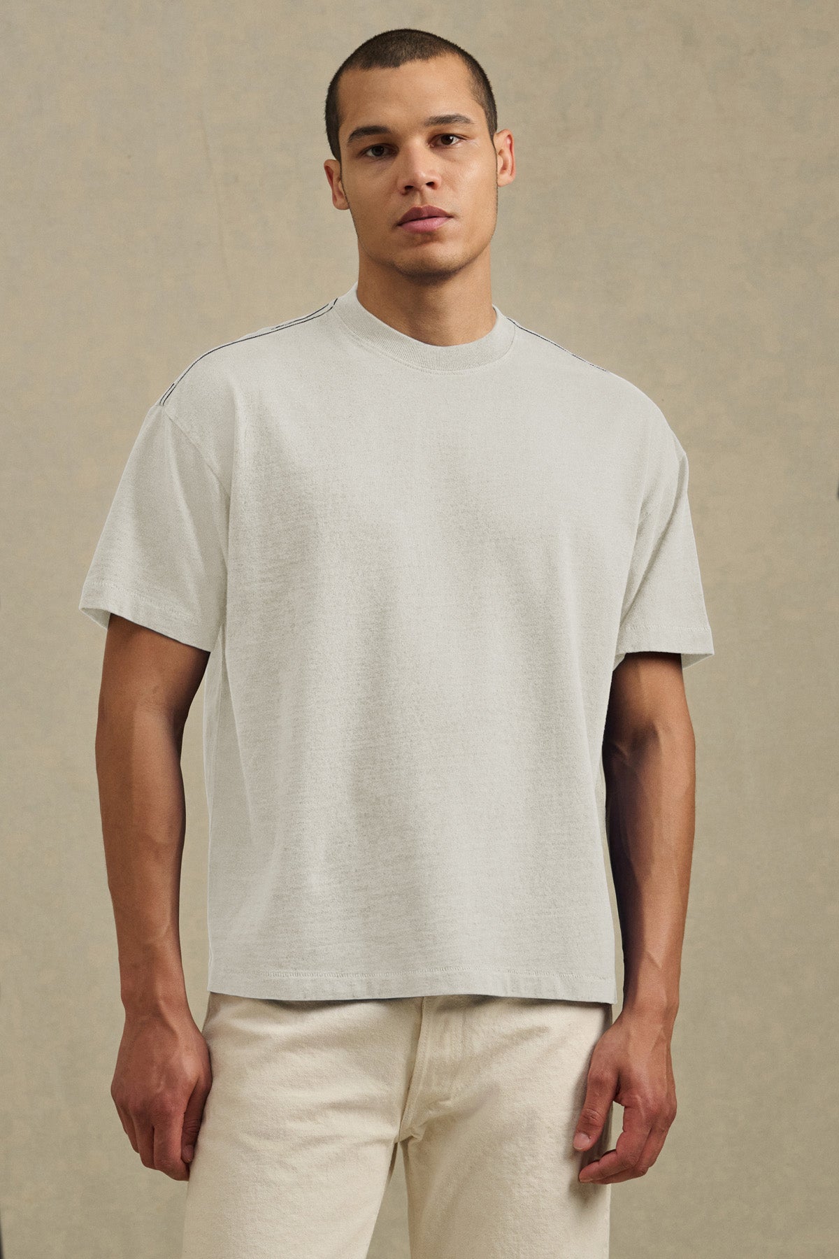 A person stands against a neutral background, wearing the ISAAC TEE from Velvet by Graham & Spencer in light beige heavier-weight cotton jersey, paired with matching pants.-41105022222529