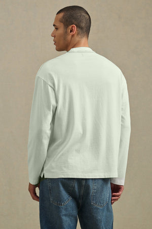 A person faces away, wearing Velvet by Graham & Spencer’s THEO TEE—a relaxed fit, heavier-weight jersey long-sleeve shirt—paired with blue jeans, set against a plain beige background.