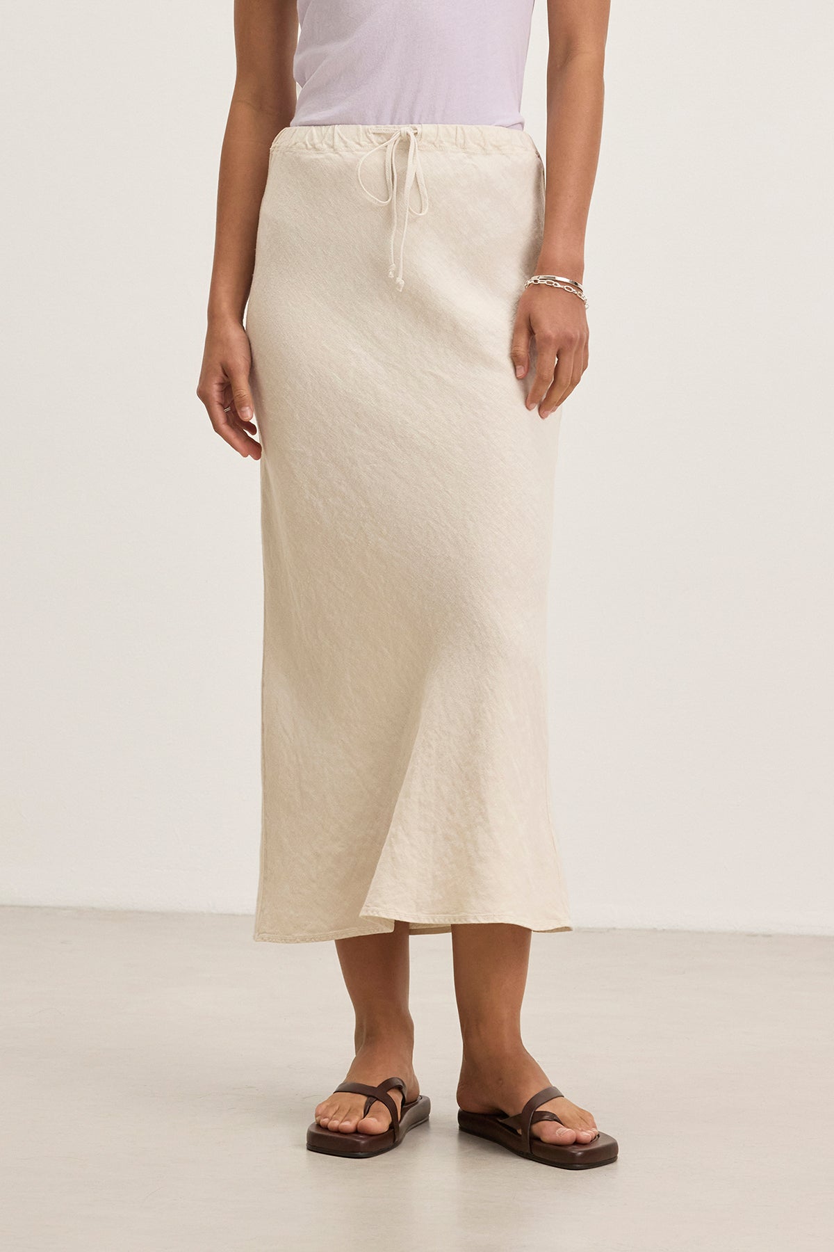 Indoors, a person dons the BEKA HEAVY LINEN SKIRT by Velvet by Graham & Spencer in beige, paired with a crisp white top.-38662641123521
