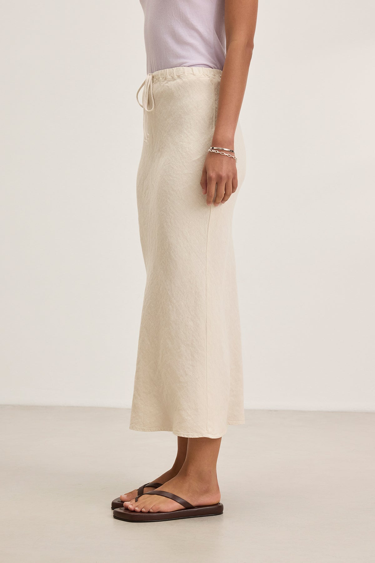 A person in a white top and BEKA HEAVY LINEN SKIRT by Velvet by Graham & Spencer, paired with flip-flops, stands against a plain background.-38662641156289