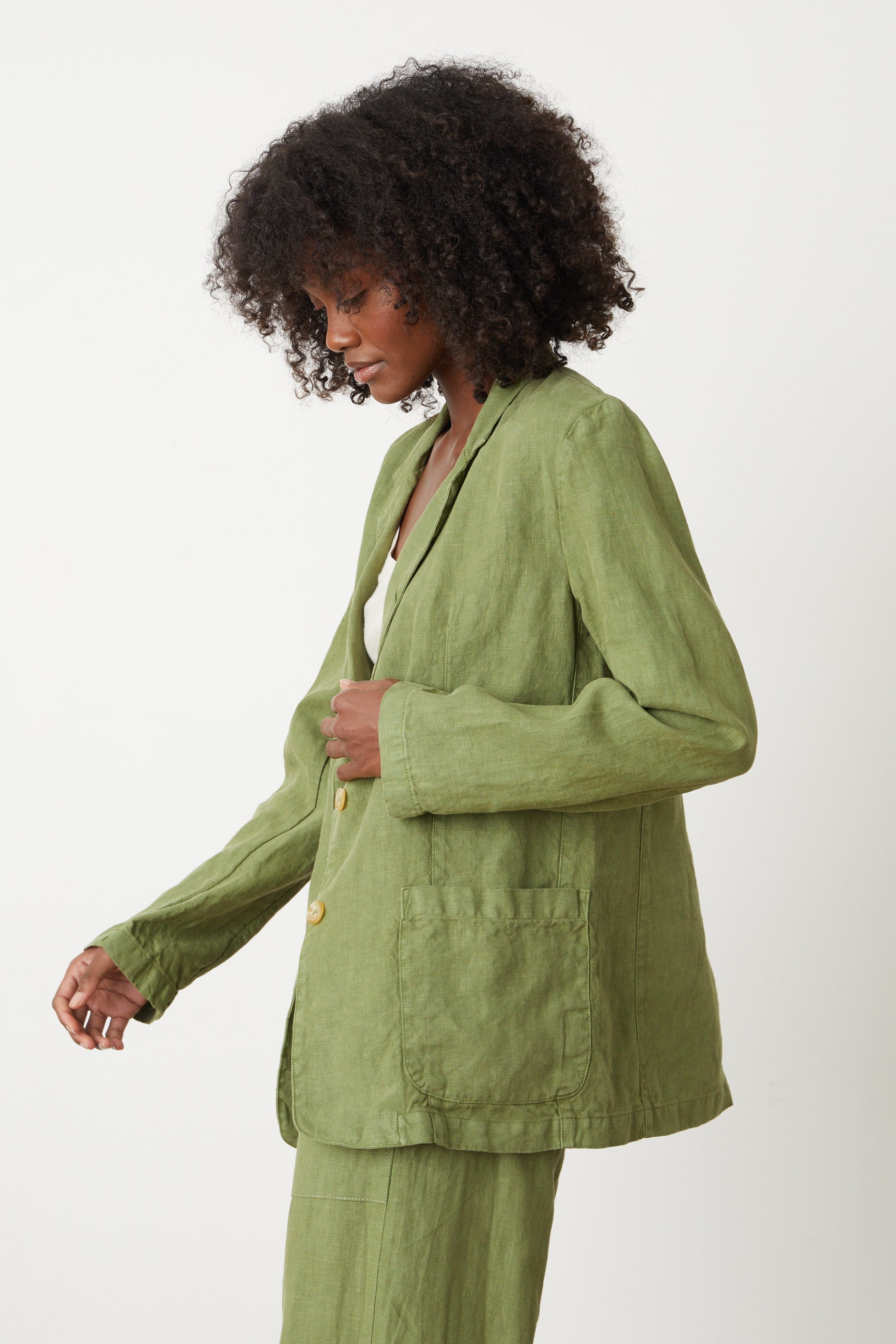   A woman wearing a tailored green CASSIE HEAVY LINEN BLAZER by Velvet by Graham & Spencer with cool-girl style. 