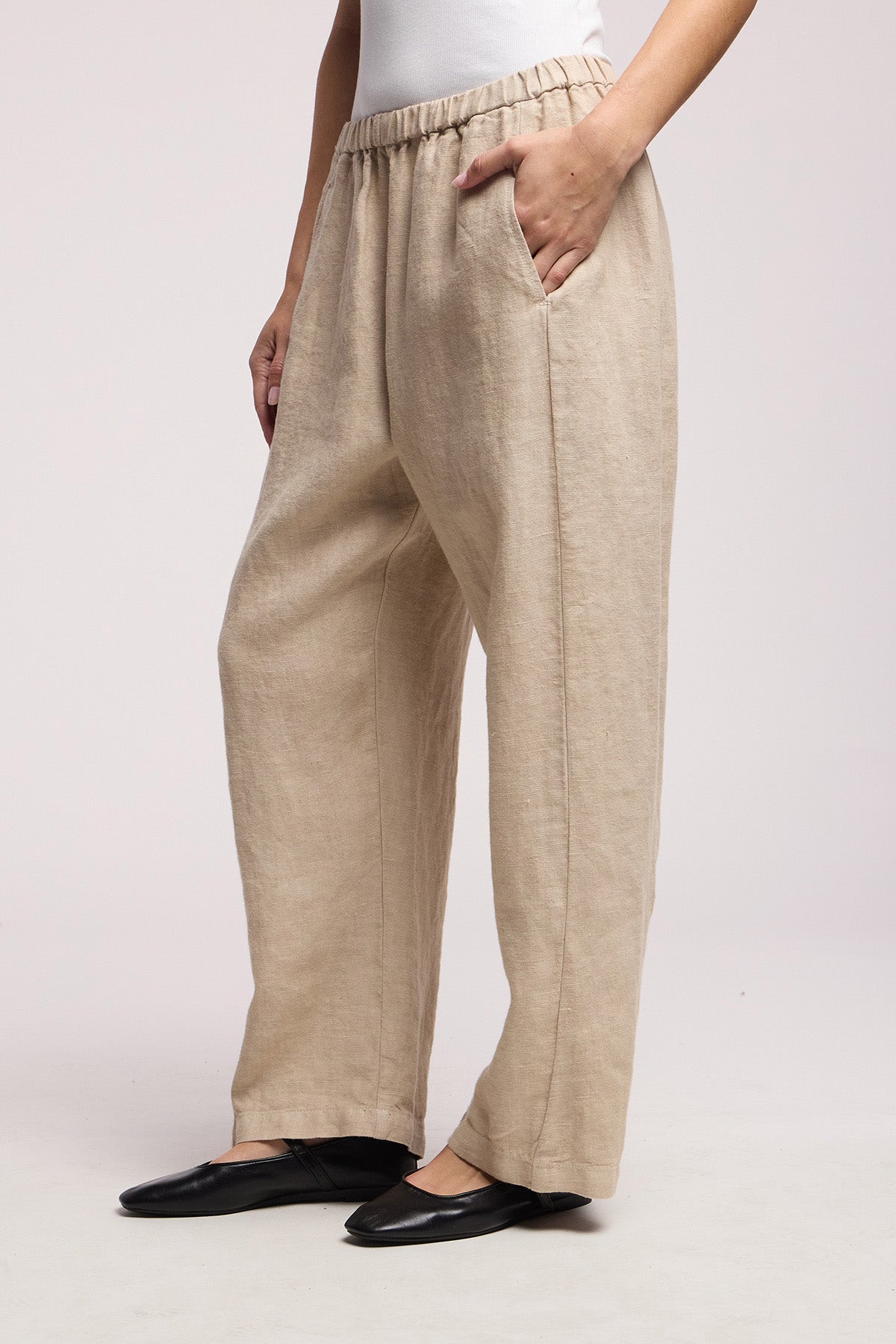 A person wears the CELINE HEAVY LINEN PANT by Velvet by Graham & Spencer—wide leg, cropped beige linen pants with an elastic waist and side pockets—paired with a white top and black flats.