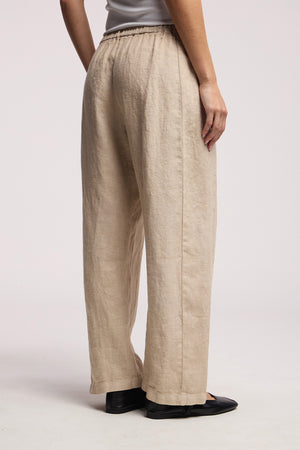 A person wears the CELINE HEAVY LINEN PANT by Velvet by Graham & Spencer—beige, wide leg, cropped pants with an elastic waist—paired with black shoes on a neutral background.