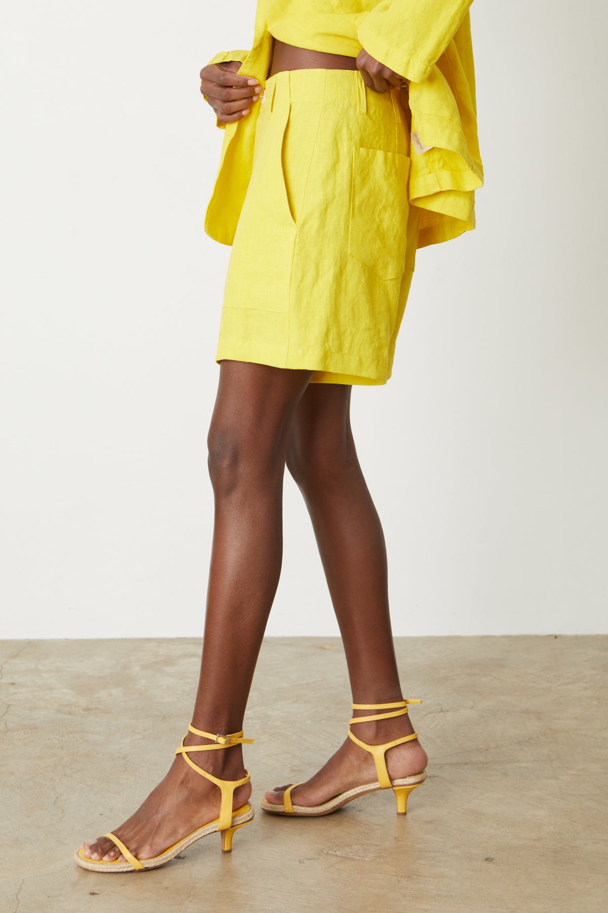 A woman wearing a yellow top and the Velvet by Graham & Spencer Fallon Heavy Linen Shorts with zipper and button closure, made of heavy linen fabric, for summer.-35204862869697