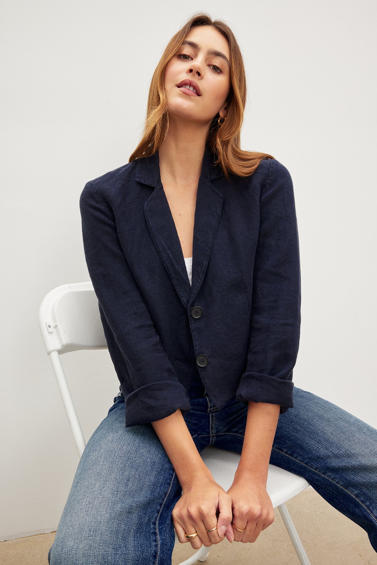 A woman is sitting on a chair wearing jeans and a Velvet by Graham & Spencer FINLEY HEAVY LINEN CROPPED BLAZER.-35982562787521