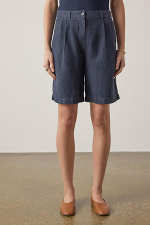 A woman stands wearing Velvet by Jenny Graham's LARCHMONT HEAVY LINEN SHORT and tan loafers, focusing on the lower half of the body against a neutral background.