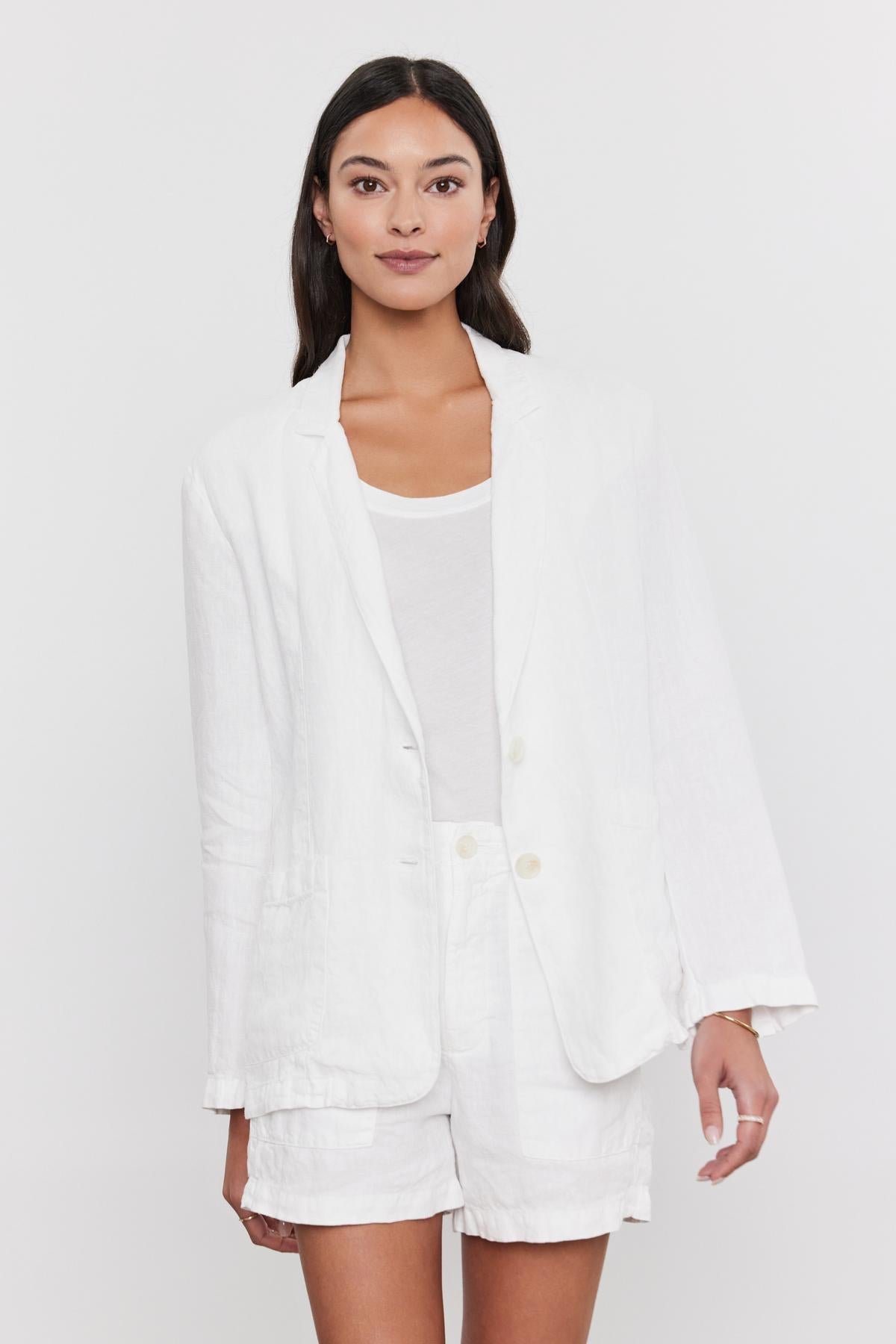 A woman in a spring suit consisting of a Velvet by Graham & Spencer LENNY HEAVY LINEN BLAZER and shorts set, paired with a white t-shirt, standing against a plain background.-36910096318657