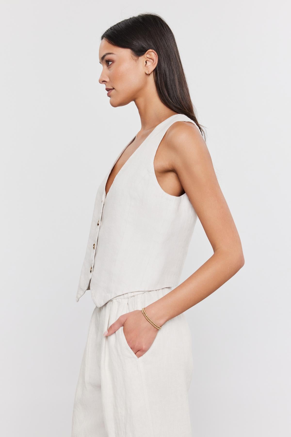   Profile view of a woman wearing a sleeveless, four-button front MYLIE HEAVY LINEN VEST by Velvet by Graham & Spencer. She is looking to the left with her hair pulled back, presenting a polished look. 