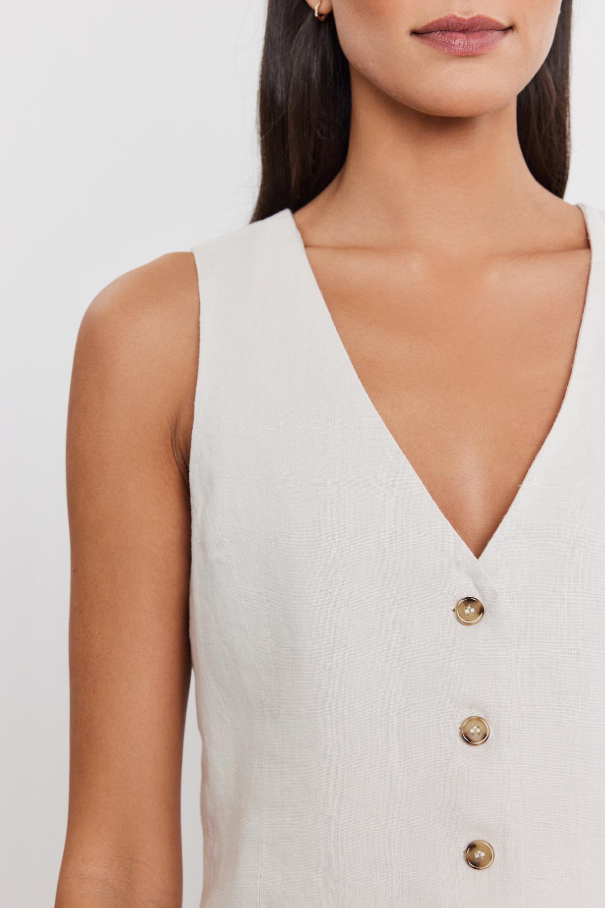   Close-up of a woman wearing a white sleeveless v-neck MYLIE HEAVY LINEN VEST by Velvet by Graham & Spencer with a four-button front. Only the lower part of her face and torso are visible. 