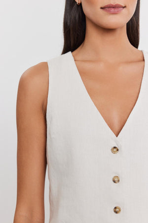 Close-up of a woman wearing a white sleeveless v-neck MYLIE HEAVY LINEN VEST by Velvet by Graham & Spencer with a four-button front. Only the lower part of her face and torso are visible.