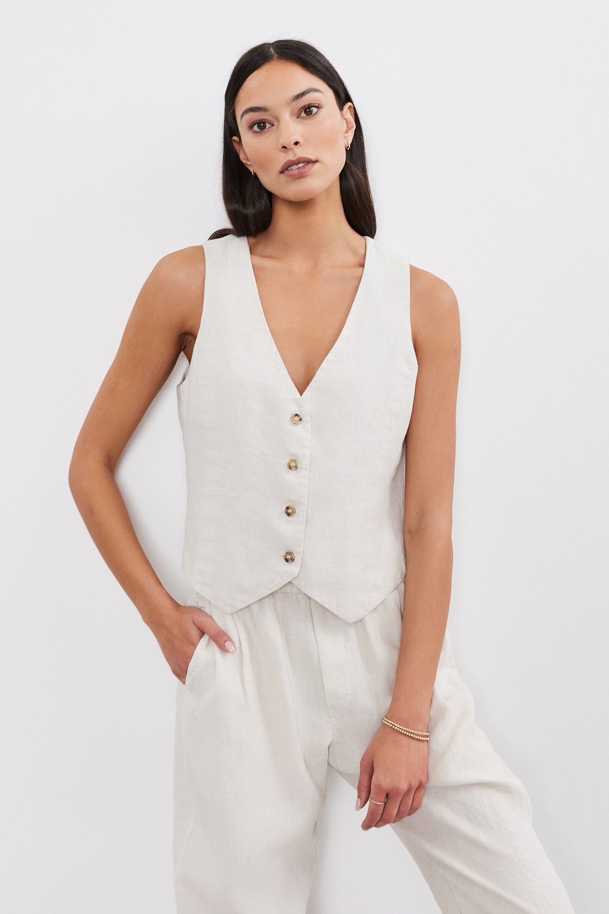   A woman wearing a beige sleeveless top and a Velvet by Graham & Spencer Mylie Heavy Linen Vest with a four-button front stands with her hands in her pockets, looking directly at the camera. 