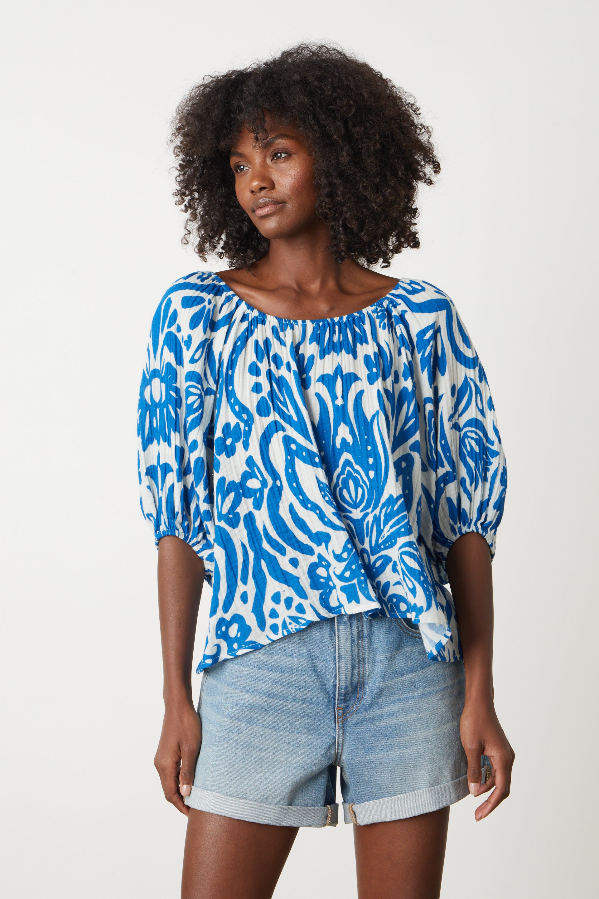   The model is wearing a Velvet by Graham & Spencer Candice Printed Cotton Gauze Top in bold blue and white print with denim shorts 
