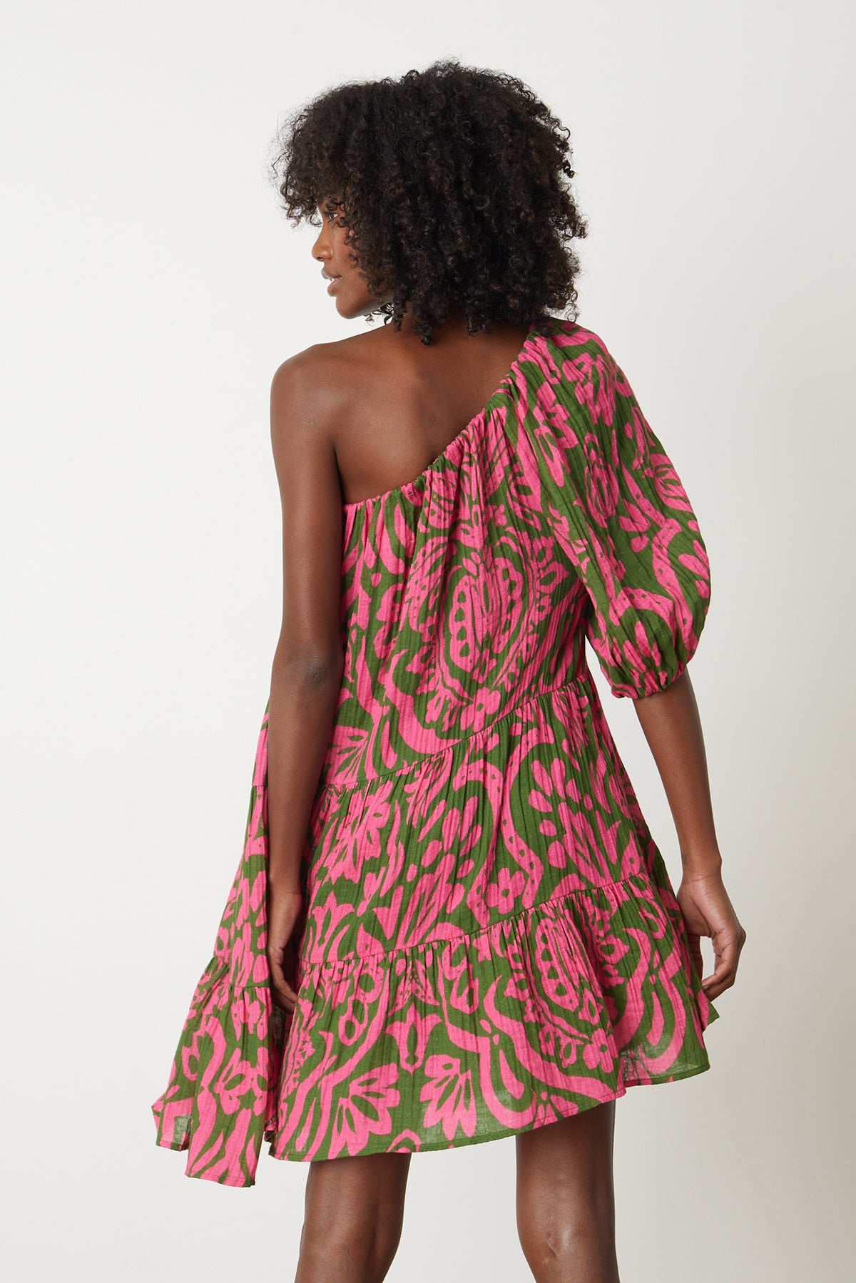   The back view of a woman wearing a Velvet by Graham & Spencer Gretchen Printed One Shoulder Dress in pink and green print. 