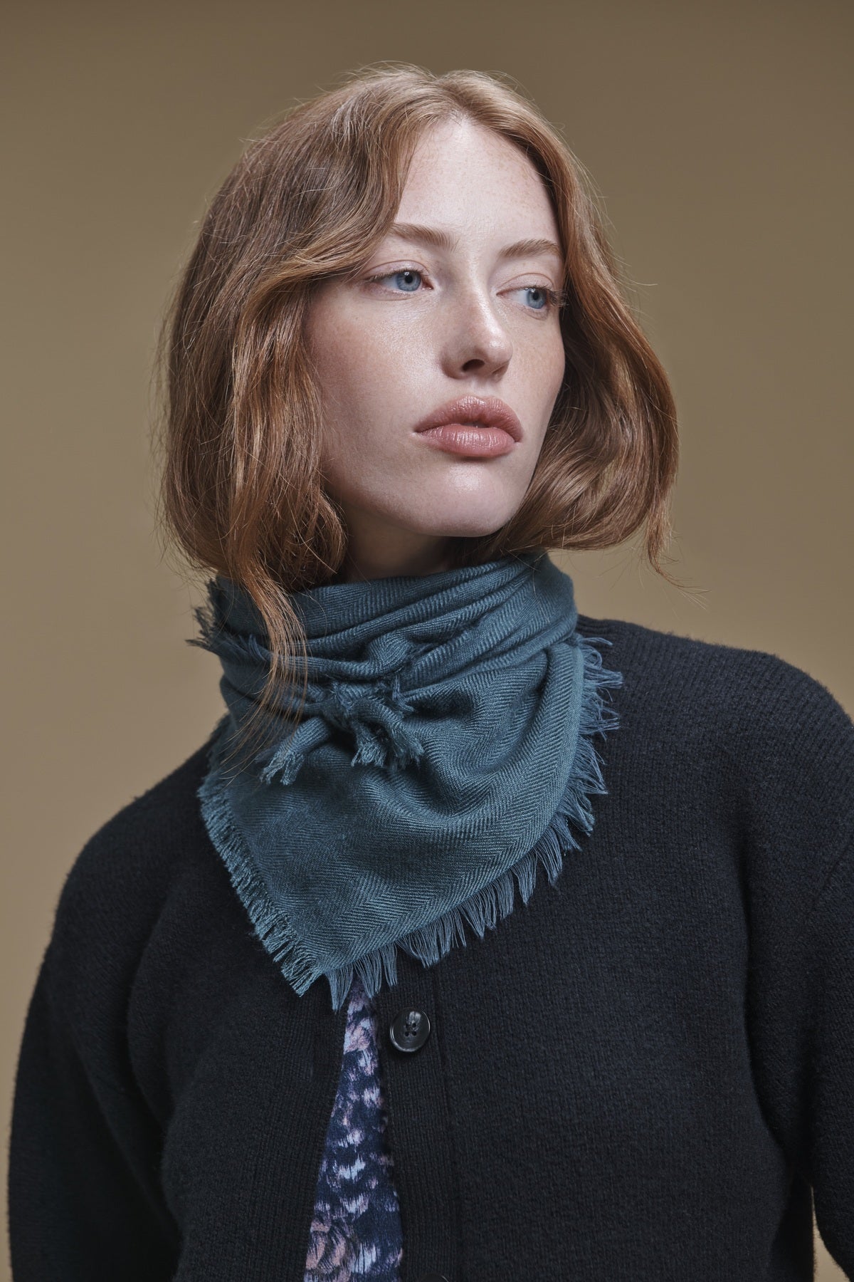 A person wears a teal triangular SUMMER CASHMERE HERRINGBONE SCARF by Velvet by Graham & Spencer, featuring a herringbone pattern and frayed edges tied around their neck.-46491217494209