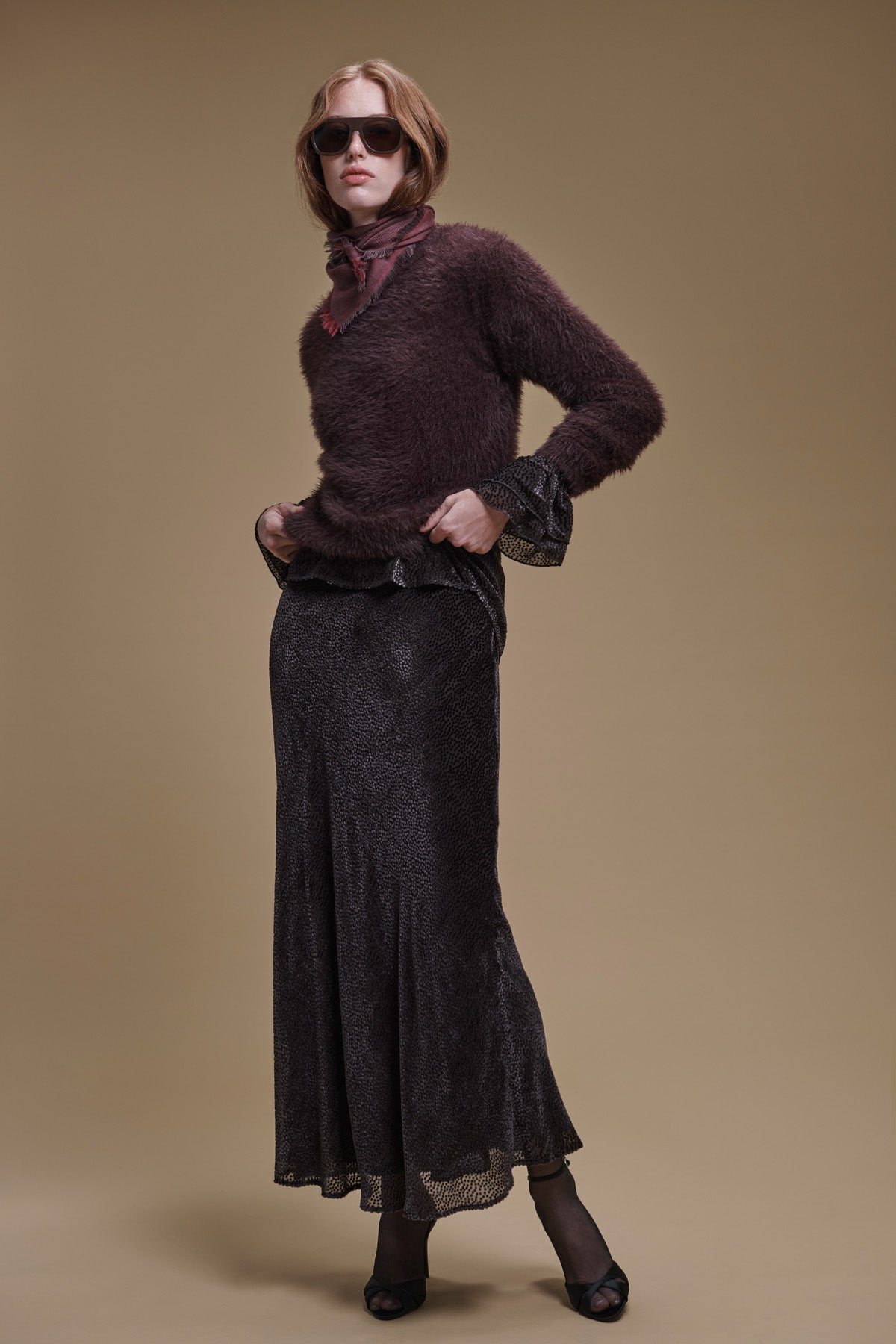 A person wearing a fuzzy dark brown sweater and a Velvet by Graham & Spencer QUINN DEVORE DOT SKIRT, which is a bias-cut maxi in a dark micro-dot print with a ruffled hem.