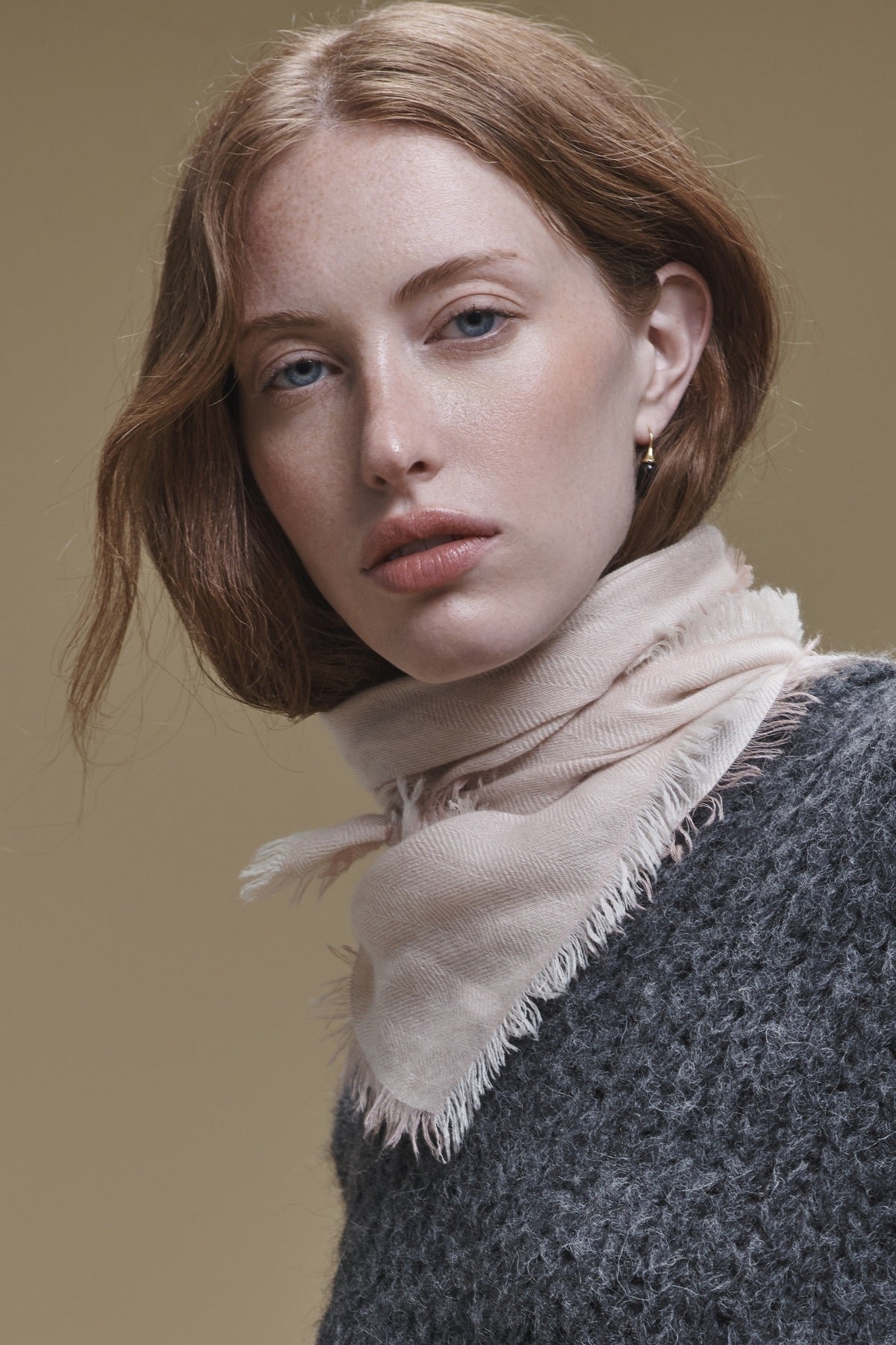A person wearing a pale pink fringed SUMMER CASHMERE HERRINGBONE SCARF tied around their neck.-46491214184641