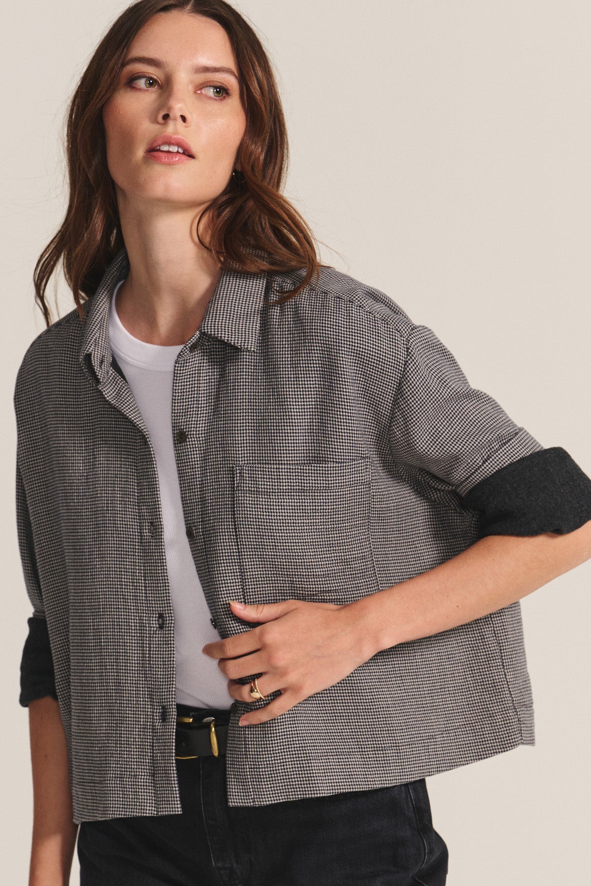 A woman wearing the ADELINE SHIRT by Velvet by Graham & Spencer over a white t-shirt, with black pants and a black belt, stands against a neutral background.
