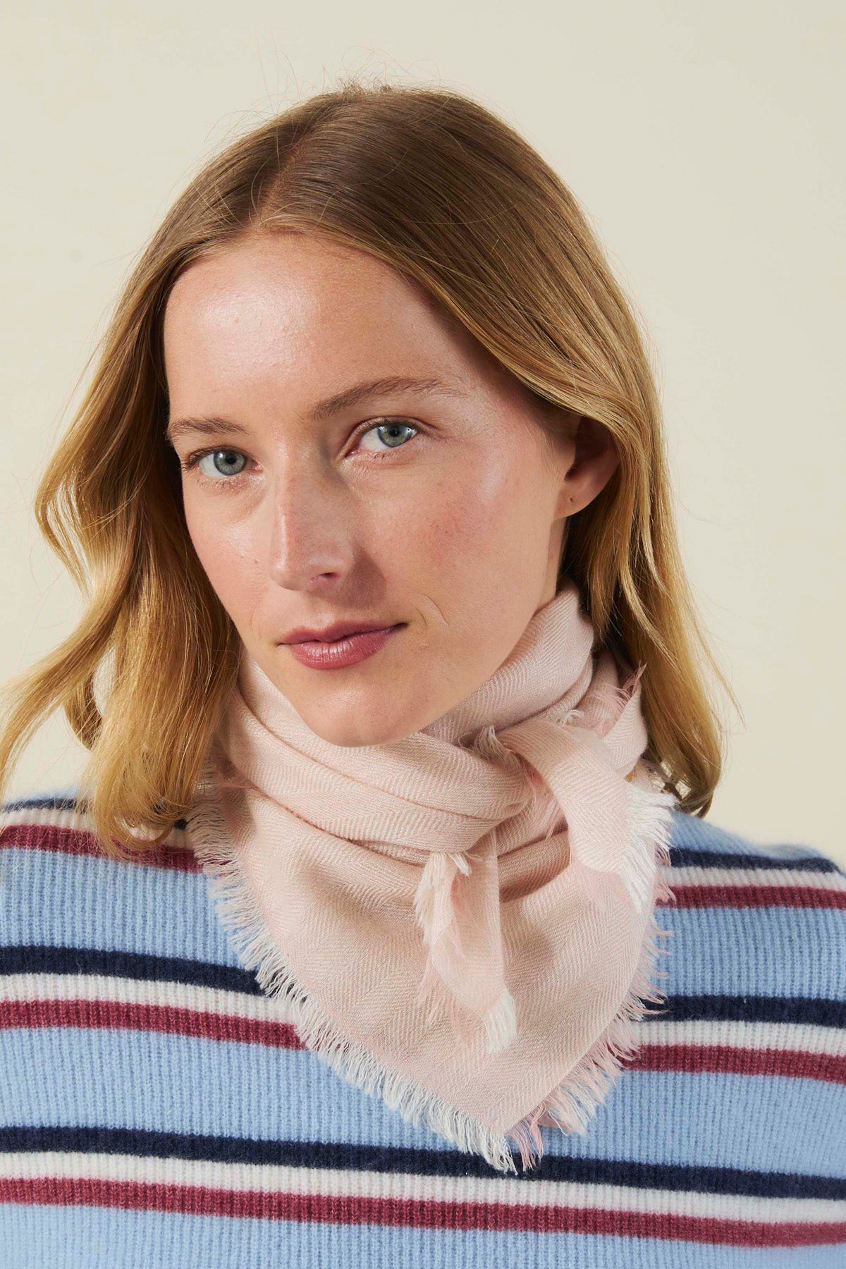 A person wearing a light pink, fringed SUMMER CASHMERE HERRINGBONE SCARF by Velvet by Graham & Spencer tied around their neck.-46490700120257