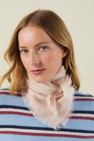 A person wearing a light pink, fringed SUMMER CASHMERE HERRINGBONE SCARF by Velvet by Graham & Spencer tied around their neck.