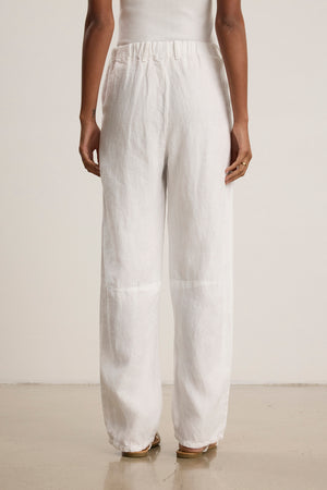 A person, seen from behind, stands on a light floor against a plain background wearing Velvet by Graham & Spencer’s TAYLOR HEAVY LINEN PANT in white with a matching white top.