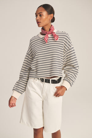 Model wears the ISABELLE PULLOVER by Velvet by Graham & Spencer—black and white stripes—paired with white shorts, black belt, and a red patterned neck scarf, set against a plain background.