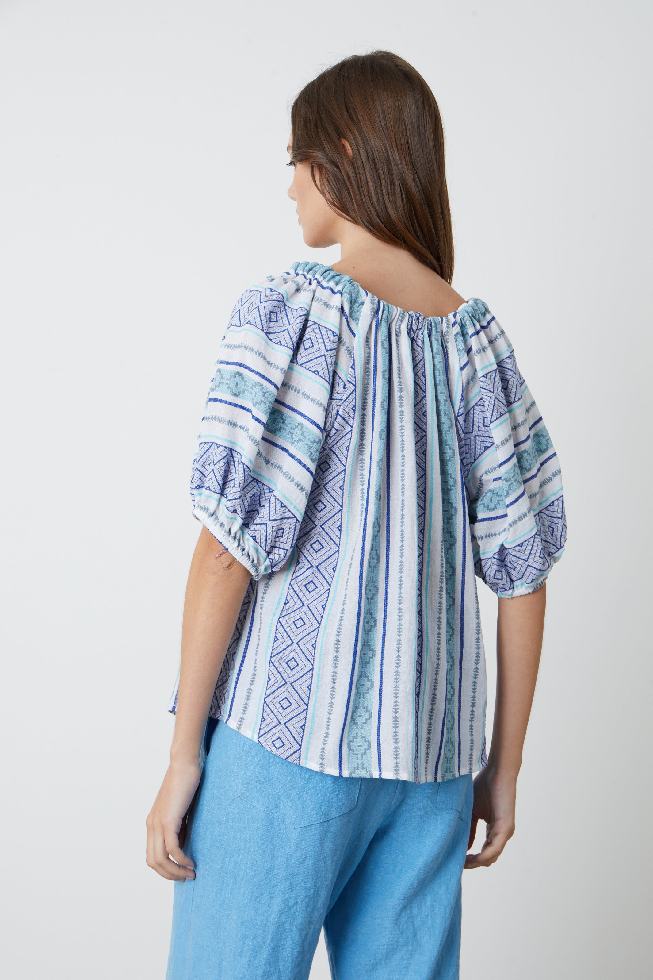   The back view of a woman wearing a Velvet by Graham & Spencer KIMMY JACQUARD BOHO TOP in blue and white jacquard print. 