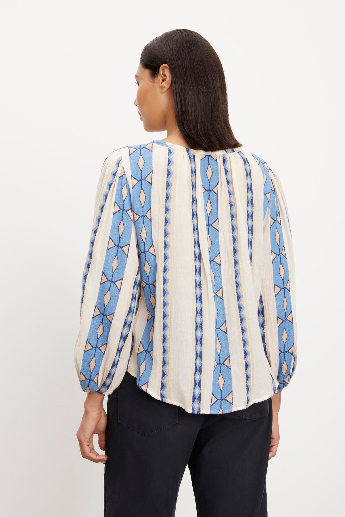 The back view of a woman wearing a Velvet by Graham & Spencer NANNI JACQUARD V-NECK BLOUSE with blue and white stripes.-35702114943169