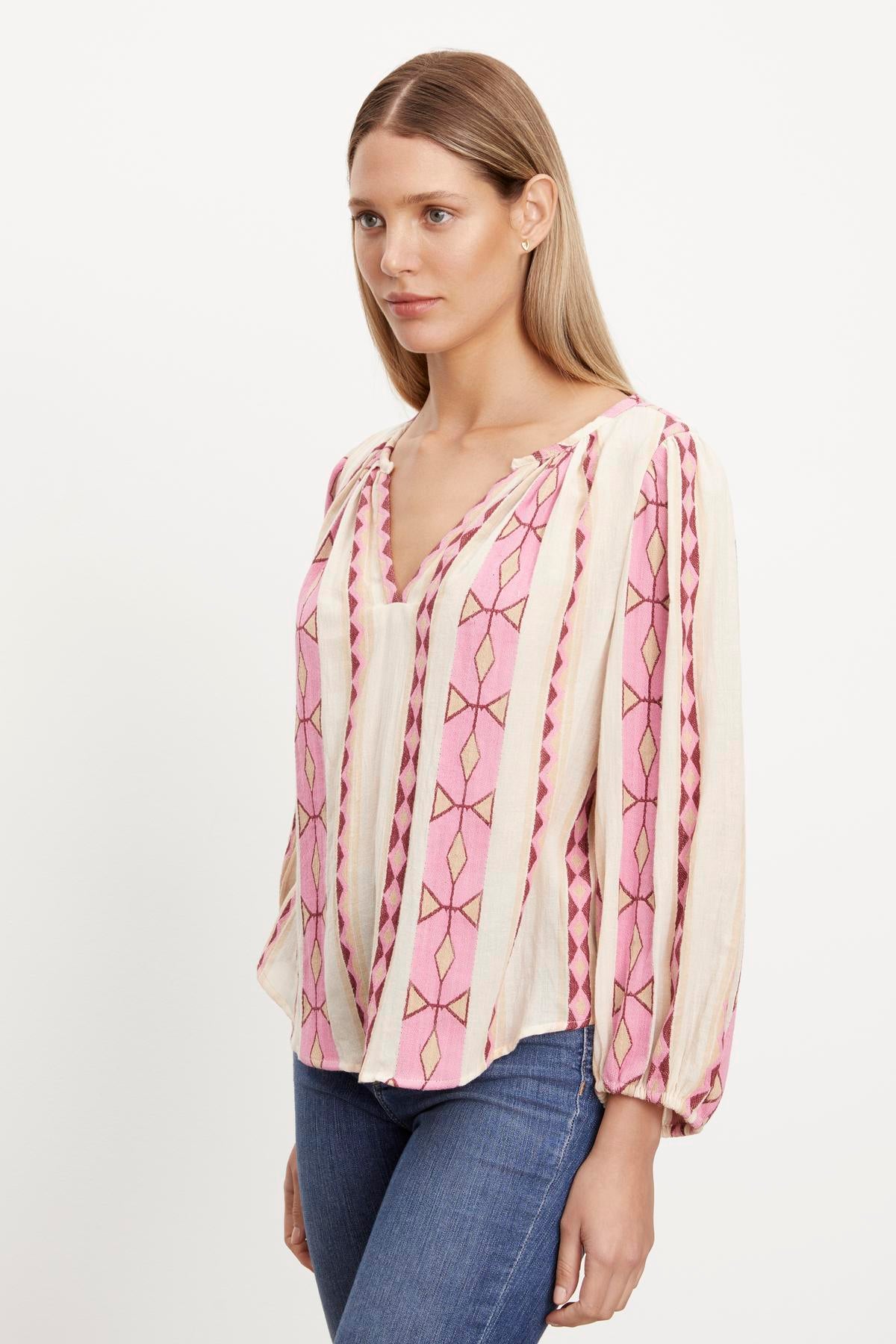   The model is wearing a pink and white embroidered NANNI JACQUARD V-NECK BLOUSE with elastic cuffs and a v-neckline by Velvet by Graham & Spencer. 