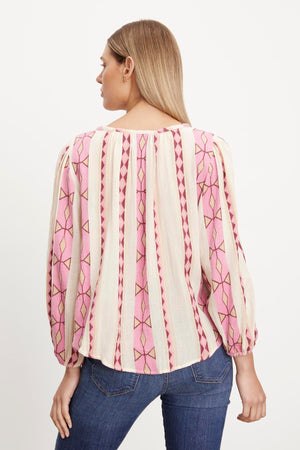 The woman is wearing a pink embroidered blouse with elastic cuffs from Velvet by Graham & Spencer.