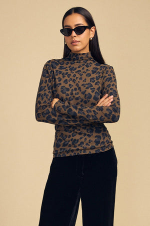 A woman wears a brown and black leopard print long-sleeved mock-neck ETTA TEE by Velvet by Graham & Spencer with her arms crossed.