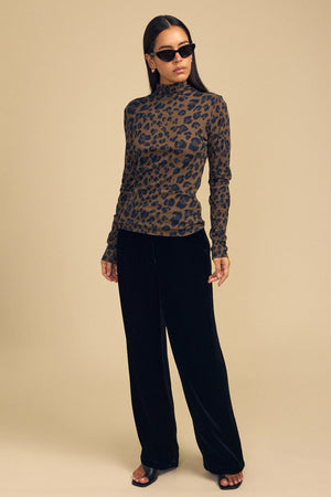 Model wearing a long-sleeved, high-neck brown leopard print ETTA TEE by Velvet by Graham & Spencer and black wide-leg trousers.