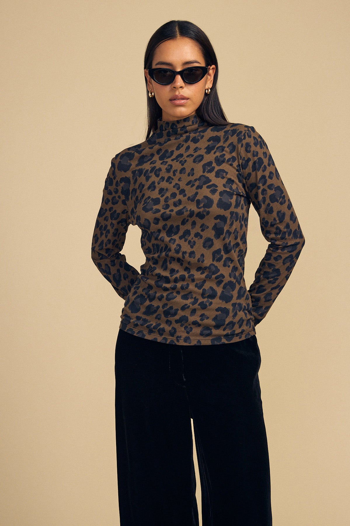 A person wearing a Velvet by Graham & Spencer ETTA TEE in a long-sleeved, brown and black leopard-print mock-neck style with black trousers.-46288349069505