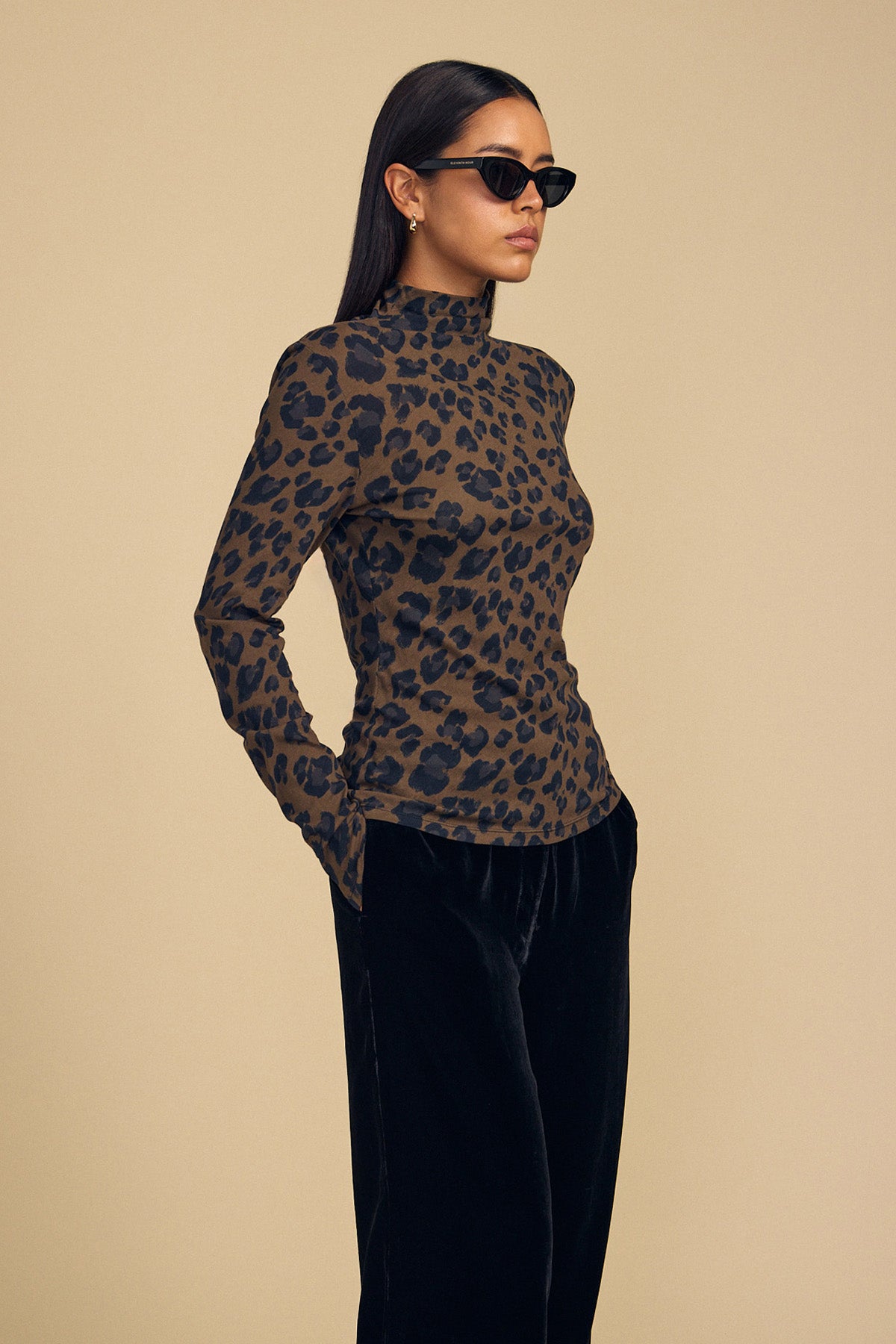 A woman wearing a Velvet by Graham & Spencer ETTA TEE in a long-sleeved, brown and black leopard-print mock-neck style with black pants.