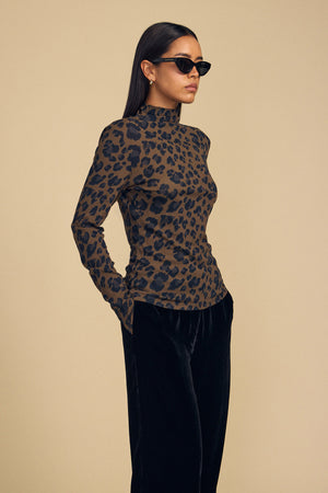 A woman wearing a Velvet by Graham & Spencer ETTA TEE in a long-sleeved, brown and black leopard-print mock-neck style with black pants.