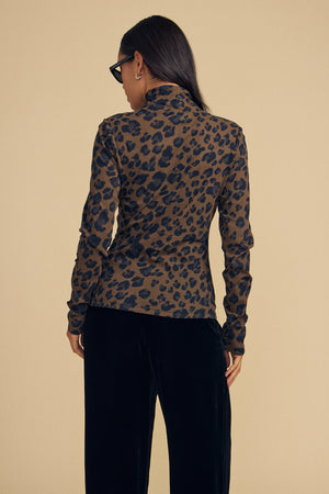 A person seen from behind wears a Velvet by Graham & Spencer ETTA TEE, featuring a brown mock-neck top with a black leopard print and dark pants.